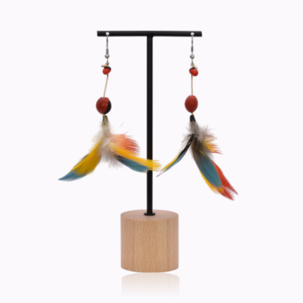 Handcrafted colorful feather earrings displayed on a wooden and black metal stand, featuring vibrant yellow, red, and blue feathers, red huayruro seeds, and sterling silver hooks